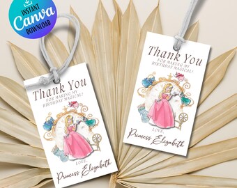 以下が含まれることがあります： プリンセスのイラストと「Thank You For Making My Birthday Magical!」の文字が入った白いギフトタグが2つ。 プリンセスはピンクのドレスを着ています。 タグには紐がついており、ニュートラルな背景に配置されています。