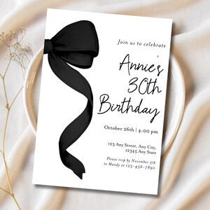 May include: Black and white birthday invitation with a black bow on the left side. The text reads "Join us to celebrate Annie's 30th Birthday, October 26th | 4:00 pm, 123 Any Street, Any City, 12345 Any State, Please RSVP by November 5th to Mandy at 123-456-7890."