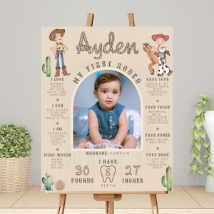 May include: A wooden sign featuring a baby's photo, cowboy and cowgirl illustrations, and text. The sign reads "Ayden, My First Rodeo." It includes the baby's weight, teeth, and height, which is 68.58 cm.
