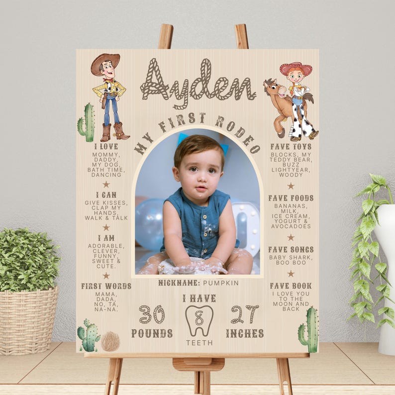 May include: A wooden sign featuring a baby's photo, cowboy and cowgirl illustrations, and text. The sign reads "Ayden, My First Rodeo." It includes the baby's weight, teeth, and height, which is 68.58 cm.