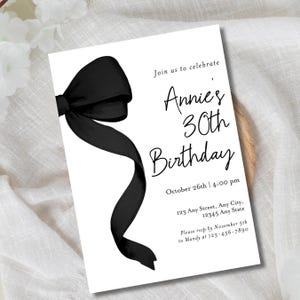 May include: Black and white birthday party invitation with a black bow on the left side. The invitation reads "Join us to celebrate Annie's 30th Birthday" with the date and time "October 26th | 4:00 pm" and the address "123 Any Street, Any City, 12345 Any State". The RSVP information is "Please rsvp by November 5th to Mandy at 123-456-7890".