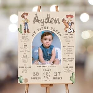 May include: A wooden sign with a photo of a baby boy, cowboy and cowgirl illustrations, and text. The sign says "My First Rodeo" and includes the baby's name, favorite things, and measurements: 13.6 kg, 8 teeth, and 68.6 cm.
