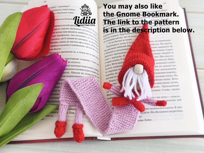 May include: A knitted gnome bookmark with a red hat, white beard, and a long light purple body resting on an open book. Beside the book are red and purple tulip flowers. The text on the page reads: You may also like the Gnome Bookmark.