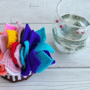 Brightly colored knitted flower mats folded together and stored inside a small handknit basket next to a glass cup.