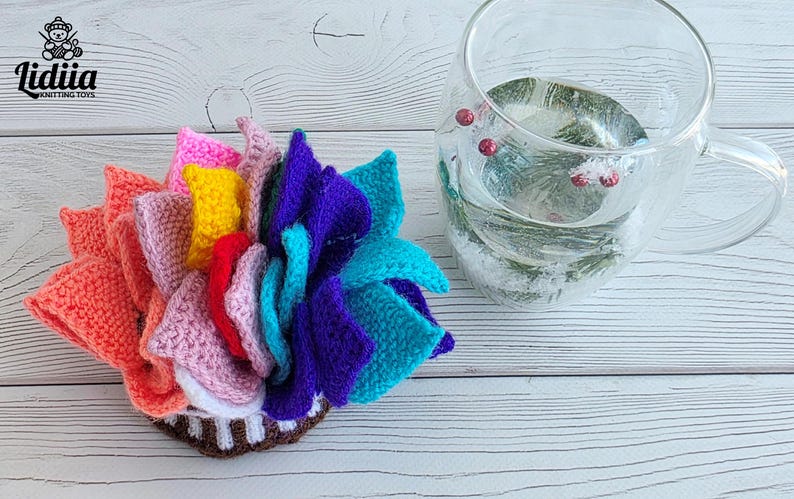 Brightly colored knitted flower mats folded together and stored inside a small handknit basket next to a glass cup.