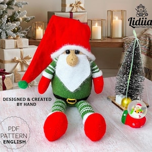 Puede incluir: Un juguete de gnomo tejido a mano con un gorro rojo alto, cuerpo verde con cinturón negro y brazos y piernas a rayas. El gnomo tiene una barba blanca y una nariz color canela. El texto dice: DESIGNED & CREATED BY HAND y PDF PATTERN ENGLISH.