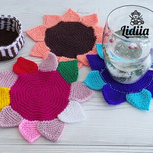 Flat lay of three vibrant flower-shaped knitted coasters and a striped brown and white storage basket on a white wooden background.