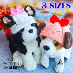 May include: Two soft toy dogs wearing knitted hats with bows. One is black and white with a white hat and pink bow. The other is white, brown, and tan with a pink hat and red bow. The image includes the text "3 SIZES" and "PDF PATTERN ENGLISH".