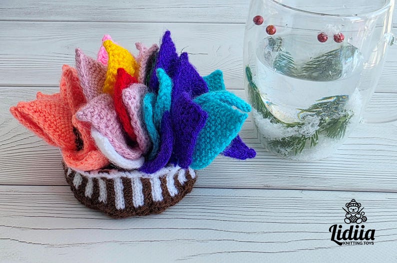 Brightly colored knitted flower mats folded together and stored inside a small handknit basket next to a glass cup.