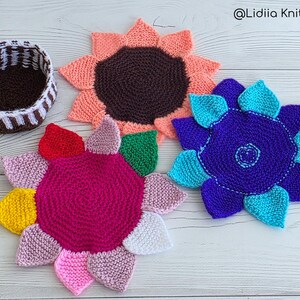 Flat lay of three vibrant flower-shaped knitted coasters and a striped brown and white storage basket on a white wooden background.