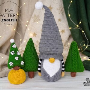 Könnte beinhalten: Ein gestrickter Wichtel mit hoher grauer Mütze, weißem Bart und gelber Nase, flankiert von drei grünen Strickbäumen. Ein Baum hat weiße Schneeflocken-Applikationen, einer ein Zopfmuster und einer steht auf einem gelben Sockel. Text PDF PATTERN ENGLISH.