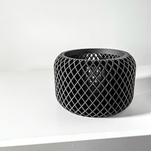Könnte beinhalten: Ein schwarzer, geometrischer, zylindrischer Pflanzer mit einem rautenförmigen Gittermuster.