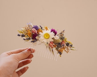 May include: A clear plastic hair comb with a variety of dried flowers attached. The flowers are in shades of purple, yellow, white, and pink.