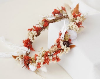 May include: A floral crown made with dried flowers in shades of white, orange, and brown. The crown is made with a variety of flowers, including baby's breath, dried grasses, and small orange flowers.