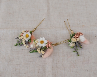 May include: Two floral hair pins with white daisies, pink accents, and gold wire stems. The pins feature dried flowers and greenery, creating a delicate and natural look. Perfect for weddings or special occasions.
