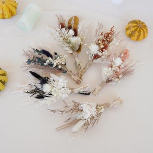 May include: Assortment of dried flower bouquets in various colours and textures, including white, brown, beige, and orange. The bouquets are tied with twine and feature dried grasses, pampas grass, and other dried flowers.