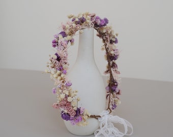 May include: A purple and white dried flower crown with a white lace ribbon.