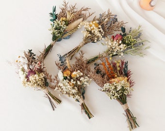 May include: Assortment of dried flower bouquets in various colors, including white, yellow, orange, and brown. The bouquets are tied with twine and are ready to be used as wedding or event decorations.