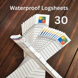 Puede incluir: Un conjunto de 30 hojas de registro impermeables blancas abanicadas sobre una superficie de madera. Cada hoja de registro tiene un logotipo colorido de Official Geocache y líneas para escribir. El texto "Waterproof Logsheets" y el número "30" son visibles.