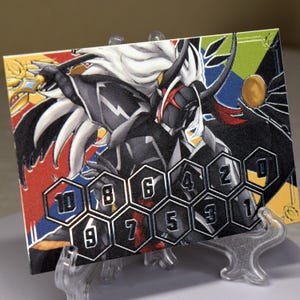 Könnte beinhalten: Eine rechteckige Karte mit einer detaillierten Illustration eines Charakters mit weißen Haaren, schwarzer Rüstung und roten Akzenten. Die Karte hat einen farbenfrohen Rand und eine Reihe nummerierter sechseckiger Formen. Die Karte wird auf einem transparenten Kunststoffständer präsentiert.