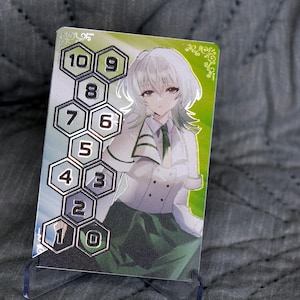 Op de afbeelding: Een zilveren kaart met een groene en witte achtergrond. De kaart heeft een zilveren honingraatpatroon met de nummers 1 tot en met 10. Op de kaart staat een anime-personage met wit haar en groene ogen.