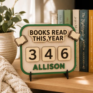 May include: Wooden book counter with the text "BOOKS READ THIS YEAR" and the name "ALLISON". The counter displays the number 346. The frame is green, and the background is white. Two small wooden book cutouts are on the frame.