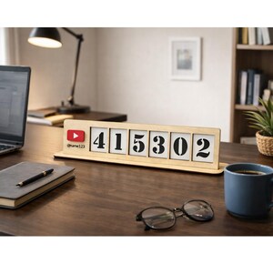 May include: A wooden desk organizer with the numbers 415302 displayed on white tiles. The organizer includes a YouTube logo and the username @name123. A laptop, notebook, pen, glasses, and a coffee mug are also on the desk.