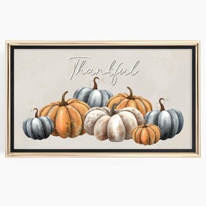 Puede incluir: Una impresión enmarcada con la palabra "Thankful" escrita en cursiva. La impresión presenta una colección de calabazas en varios tonos de azul, naranja y blanco.