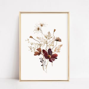 May include: A framed botanical art print featuring a bouquet of dried flowers in shades of burgundy, brown, and beige. The artwork is set against a cream background and framed in a gold-colored metal frame. The floral arrangement includes cosmos flowers and various seed heads.
