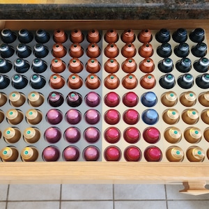 Może przedstawiać: Organizer do szuflady z różnymi kolorowymi kapsułkami kawy. Organizer jest podzielony na sekcje, z których każda zawiera inny kolor kapsułek. Kapsułki są ułożone w siatkę.