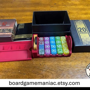 May include: A 20 Strong board game set including a black box with gold text, a rulebook, a red plastic dice tray holding multi-colored dice with various symbols, and a separate red plastic component tray. The game box lid features the text 20 STRONG.