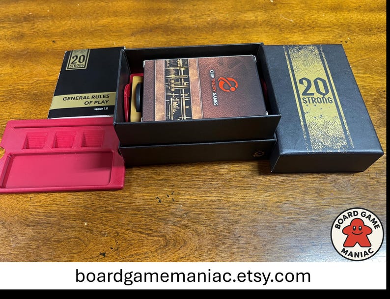 Puede incluir: Un juego de mesa 20 Strong que incluye una caja negra con texto dorado, un manual de reglas titulado General Rules of Play version 1.0, una baraja de cartas con el logo de Chip Theory Games y una bandeja de pl&aacute;stico rosa brillante con ranuras.