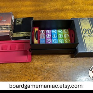 Puede incluir: Un juego de mesa 20 Strong que incluye una caja negra con texto dorado, un manual de reglas, una bandeja de pl&aacute;stico roja y una colecci&oacute;n de dados coloridos. Los dados est&aacute;n organizados en una caja de almacenamiento negra, con varios s&iacute;mbolos blancos en caras moradas, azules, verdes y amarillas. La tapa de la caja muestra el texto 20 STRONG en negrita.