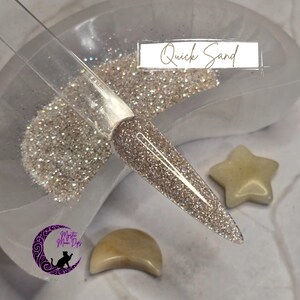 May include: A close-up of a clear container filled with a sparkly, iridescent glitter called "Quick Sand". The glitter is a light beige color with a subtle shimmer.