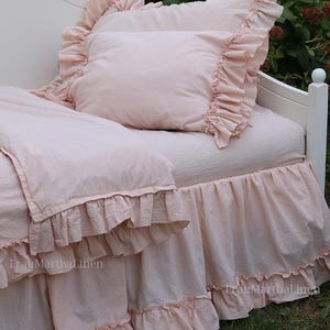 Könnte beinhalten: Ein rosa, gerüschter Bettrock mit einem passenden rosa, gerüschten Kissen auf einem weißen Bettrahmen. Das Bett steht vor einem Hintergrund aus grünem Gras.