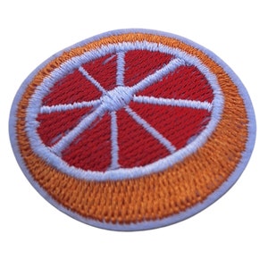 May include: A round embroidered patch with an orange peel border and a red grapefruit slice in the centre. The grapefruit slice has a white centre and white lines radiating out from the centre.