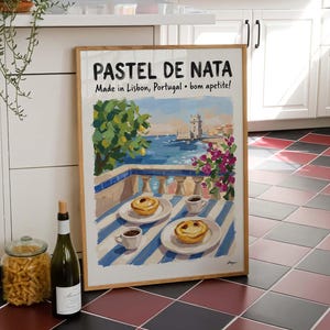 May include: A framed print of a pastel de nata pastry scene, with the text "PASTEL DE NATA Made in Lisbon, Portugal • bom apetite!" displayed in a kitchen setting. A bottle of wine and a jar of pasta are in the foreground.