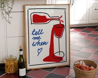 Op de afbeelding: Een ingelijst kunstprint met een rode en witte illustratie van een wijnfles die in een glas wordt gegoten. De tekst "tell me when ♥" staat in blauw onder de illustratie.