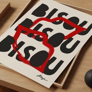 Op de afbeelding: Een zwart-witte print met het woord "Bisou" dat meerdere keren in een gestileerd lettertype wordt herhaald. Een rode hartvorm is om de woorden getekend.