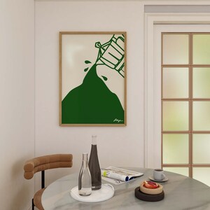 May include: A framed illustration of a green mountain with a white outline of a person pouring water from a bucket. The illustration is on a white background and the frame is wood.