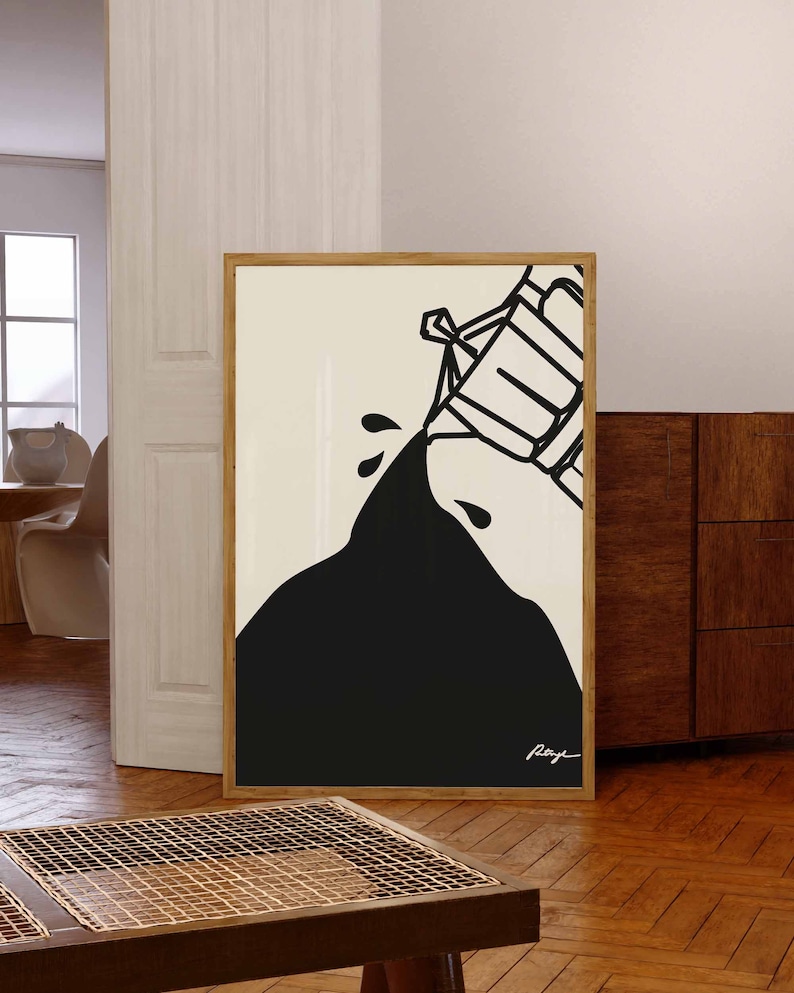 May include: Black and white abstract art print in a wooden frame. The print features a black shape pouring from a white container. The artist's signature is visible in the bottom right corner.