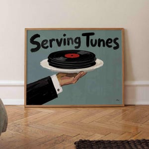 May include: A framed print featuring a hand in a black suit sleeve holding a white plate with a stack of black vinyl records. The text Serving Tunes is written in black brush-style lettering above the plate against a muted blue-green background.