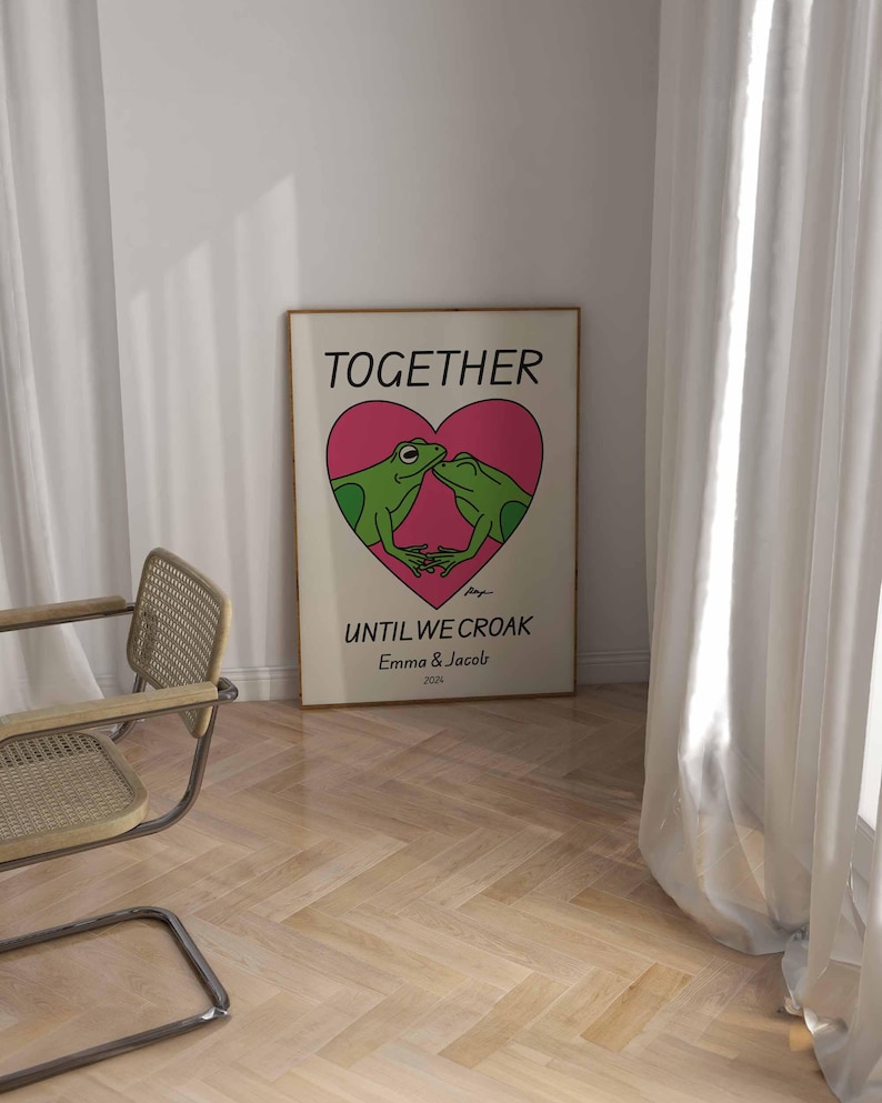 May include: A white poster with a pink heart and two green frogs kissing inside the heart. The text on the poster reads "Together Until We Croak Emma & Jacob 2024".
