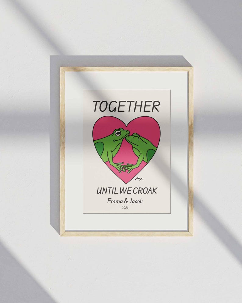 May include: A framed print with a pink heart and two green frogs kissing inside. The text reads "Together Until We Croak" with the names "Emma & Jacob" and the year "2024" below.