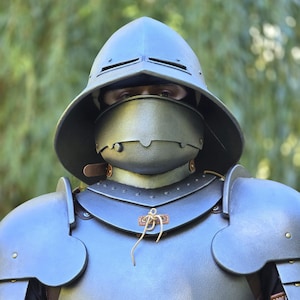 Puede incluir: Un casco sallet de metal gris oscuro con visera y una coraza a juego con hombreras. La armadura presenta remaches visibles, correas de cuero y un cordón de color claro en el centro de la pieza del pecho, proporcionando cobertura total del torso.