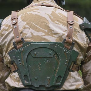 May include: A person wearing a military-style outfit, including a camouflage jacket and a green helmet. The outfit features a green chest plate with brown leather straps and accents. The overall aesthetic suggests a cosplay or costume.