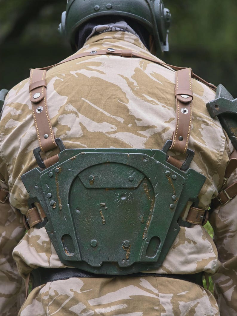 May include: A person wearing a military-style outfit, including a camouflage jacket and a green helmet. The outfit features a green chest plate with brown leather straps and accents. The overall aesthetic suggests a cosplay or costume.