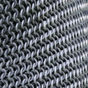 May include: Close-up of a chainmail texture. The image shows a dense pattern of interlocking, silvery-gray metal rings. The rings are arranged in rows and columns, creating a flexible, mesh-like structure. The lighting highlights the metallic sheen.
