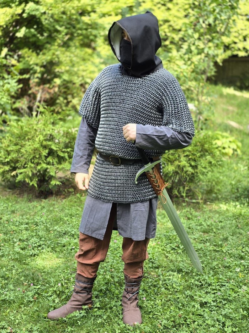 May include: A medieval costume featuring a chainmail shirt, hooded cowl, and a sword. The outfit includes a gray tunic, brown pants, and leather boots. The sword has a green blade and a brown leather-wrapped handle.