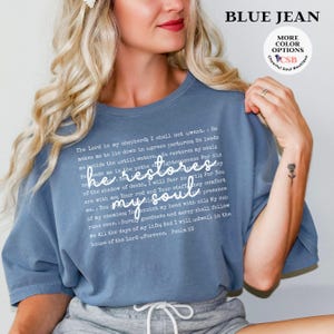 Puede incluir: Una camiseta color azul jean con el texto completo del Salmo 23 impreso en blanco, con la frase 'he restores my soul' en una letra cursiva m&aacute;s grande en el centro. La prenda cuenta con cuello redondo y mangas cortas.